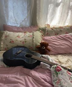 a guitar sitting on top of a bed next to pillows and a stuffed animal in the corner