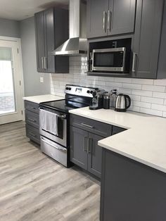 a kitchen with gray cabinets and white counter tops, stainless steel stove top oven and dishwasher