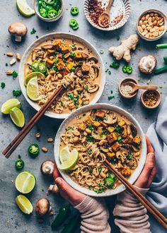 two bowls of noodles with chopsticks in front of them, surrounded by ingredients