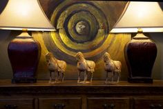 three lamps sitting on top of a wooden table next to a painting and two vases