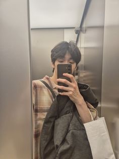 a young man taking a selfie in the mirror on his cell phone while riding an escalator