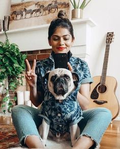 a woman is sitting on the floor with her dog in front of her and holding an electronic device up to her face