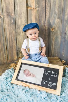 a baby in overalls and a hat sitting next to a sign