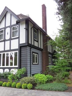 a gray and black house with white trim on the windows, bushes and trees around it