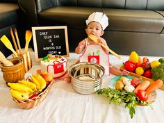 a baby is holding a wooden spoon in front of some fruits and vegetables on a table