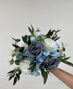 a bouquet of blue and white flowers is held by someone's hand in front of a wall