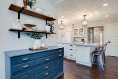 a kitchen with white cabinets and blue drawers on the countertop, along with open shelving