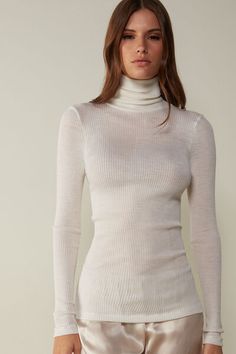 Long-sleeve high-neck tubular top made from a wool-silk blend. Elegant High Neck Tops For Winter, Elegant High Neck Winter Tops, Fitted Cream Turtleneck With Long Sleeves, Fitted Elegant Winter White Sweater, Elegant Fitted Winter White Sweater, Elegant Winter White Fine Knit Top, Elegant Winter White Turtleneck Top, Elegant Off-white Tops For Work, Fitted Cream Turtleneck For Winter