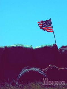 an american flag flying in the wind on top of a hill