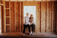 a man and woman sitting on top of a wooden floor in a room under construction