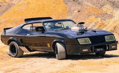 an old muscle car parked in front of a hill side with dirt on the ground