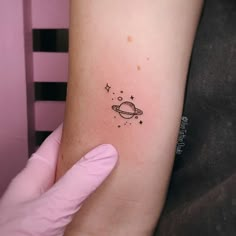 a small saturn tattoo on the left inner arm, with stars and planets around it