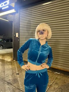 a woman with blonde hair standing in front of a garage door wearing blue pants and a crop top