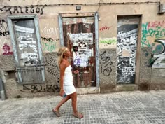 a woman walking down the street in front of some graffiti covered buildings with doors and windows