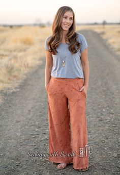 a woman standing in the middle of a dirt road with her hands on her hips