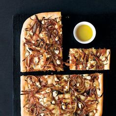 a square pizza with onions and cheese on it next to a cup of olive oil