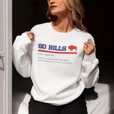 Stay warm and stylish while cheering on your favorite team with our Go Bills Definition Unisex Crewneck Sweatshirt! Crafted from high-quality fabric, this cozy sweatshirt features a unique, dictionary-inspired design that's perfect for die-hard Buffalo Bills fans. Whether you're at the stadium, lounging at home, or out with friends, this sweatshirt is a must-have addition to your Bills gear. Key Features: Premium Quality: Made with the durable and soft Gildan 18000 fabric, this sweatshirt ensure Fan Apparel Slogan Tops For Sports Events, Team Spirit Slogan Tops For Fan Gear, Team Spirit Slogan Tops For Fans, Slogan Fan Gear Tops, White Sports Fan Tops, Sports Fan Apparel Tops With Slogan, White Tops With Team Logo For Winter, White Winter Tops With Team Logo, White Winter Sports Fan Tops