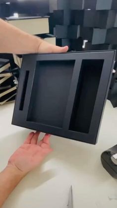 a person is holding up a small black framed object with one hand on the table