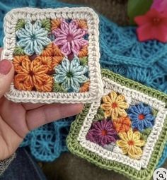 two crocheted squares with flowers on them are being held by someone's hand