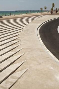 an empty parking lot next to the beach with people walking on it and one person riding a skateboard