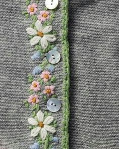 a close up of a sweater with buttons and flowers on the front, along with an attached tie