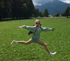 a woman running across a lush green field with mountains in the backgroung