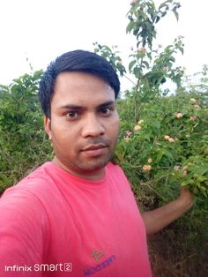 a man in a pink shirt standing next to bushes