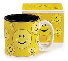 a yellow coffee mug with smiley faces on it and a box for the cup to be opened