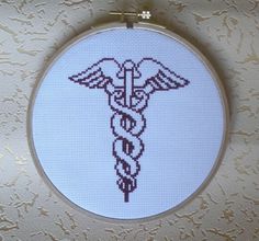 a cross stitch pattern with a cadus symbol on it