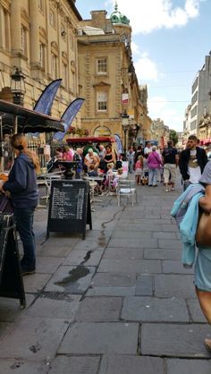 many people are walking down the street in front of some buildings and vendors on the sidewalk