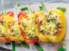 four stuffed peppers on a cutting board with green beans and cheese, ready to be eaten