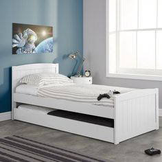 a bedroom with blue walls and a white bed in the middle, there is a skateboard laying on the floor next to it