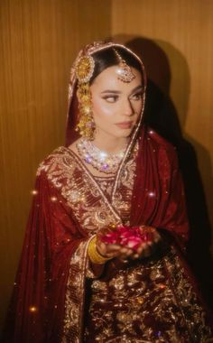 a woman in a red and gold wedding outfit holding a pink flower on her left hand