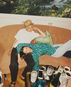 two people are laying on a couch with many items