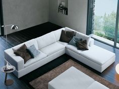 a living room with a white sectional couch and brown pillows on the floor next to a large window