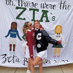 two girls are posing in front of a banner