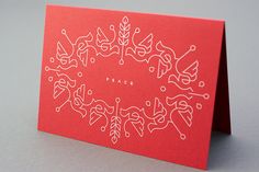 a red greeting card with white designs on the front and bottom, featuring an ornamental wreath