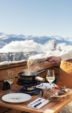 a woman pouring wine into a wok on top of a wooden table in the snow