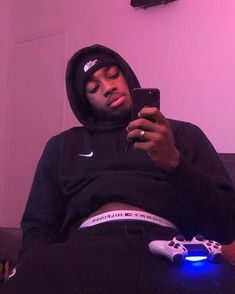 a man in a hoodie is looking at his cell phone while sitting on a couch