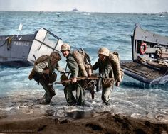 three men in the water pulling a boat out of the ocean with another man standing next to them