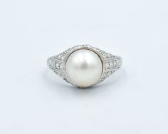 An amazing and authentic 1920's-1930's platinum pearl diamond ring. Diamonds surround the base of the pearl and taper down to the shoulders. A carved wheat design goes all the way around the band. A lovely example from the Art Deco era! The cultured 9mm pearl is a pretty cream white with less rosé tones than the pictures show. Twenty-two chunky old mine single cut diamonds total approximately 0.16 carat. The ring weighs 4.4 grams. The ring is a size 5.0. The diamonds on the side will make it dif Classic Platinum Pearl Ring, Classic Oval Pearl Ring With Center Stone, Vintage White Pearl Ring With Brilliant Cut, Classic White Platinum Pearl Ring, Classic White Pearl Ring In Platinum, Platinum Diamond Wedding Band, Pearl Diamond Ring, Wheat Design, Authentic Art