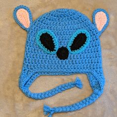 a blue crocheted hat with ears and eyes on top of a bed sheet