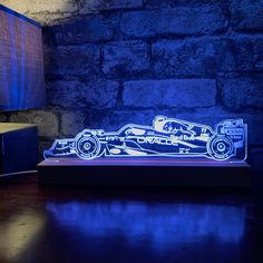 an illuminated race car sits on a table in front of a brick wall and lamp