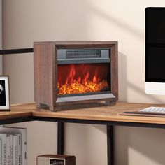 a computer desk with a monitor, keyboard and fire in the fireplace that is lit