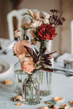 two vases filled with flowers sitting on top of a white tablecloth covered table