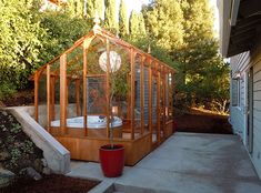 a small wooden greenhouse sitting on the side of a house next to some trees and bushes