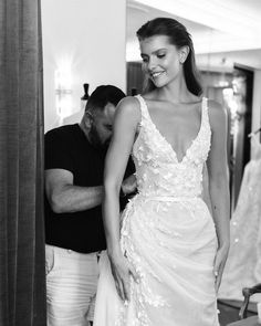 a woman in a wedding dress standing next to a man looking at the bride's dress