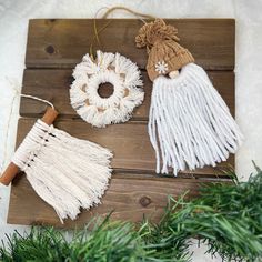 two white tasseled ornaments are hanging on a wooden board