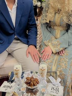 a man and woman sitting next to each other in front of a table filled with desserts