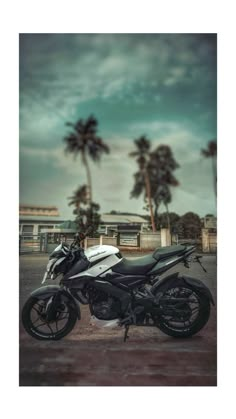 a motorcycle parked in front of palm trees on a cloudy day with dark clouds overhead